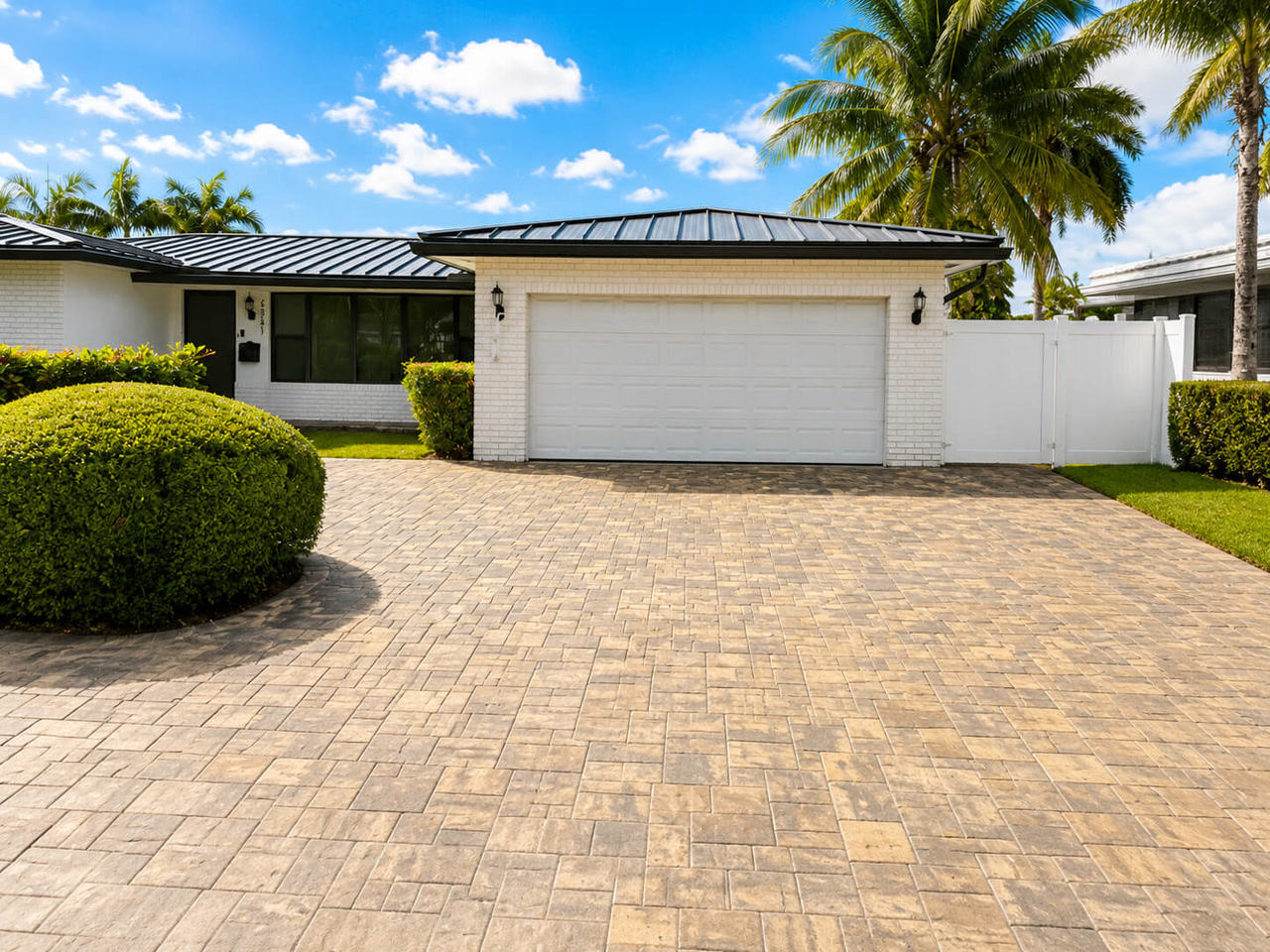 Beige running bond paver driveway at a Juno Beach home with a black standing seam metal roof