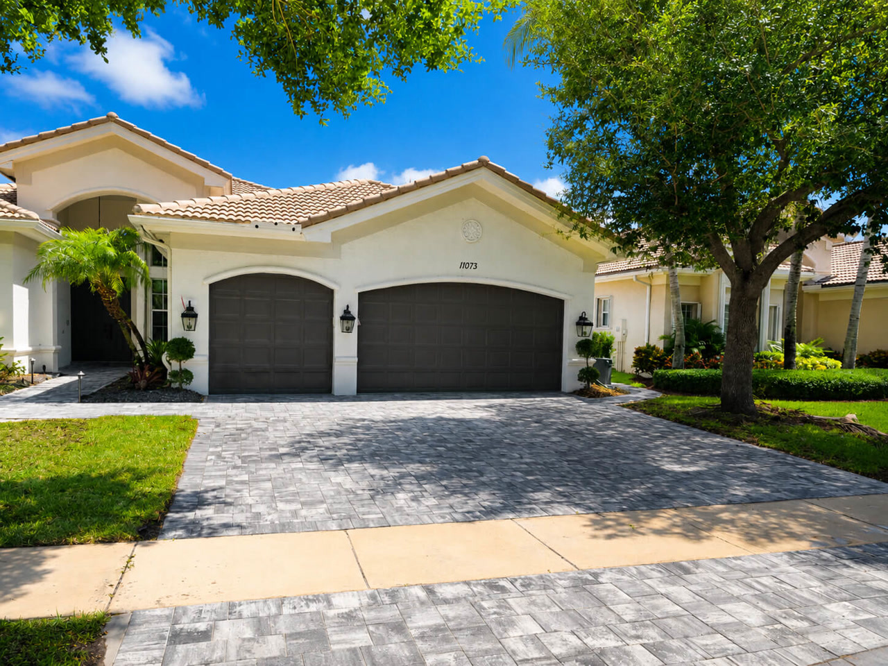 Finished gray paver driveway spanning a three car garage at a Mediterranean style Lake Worth Beach residence