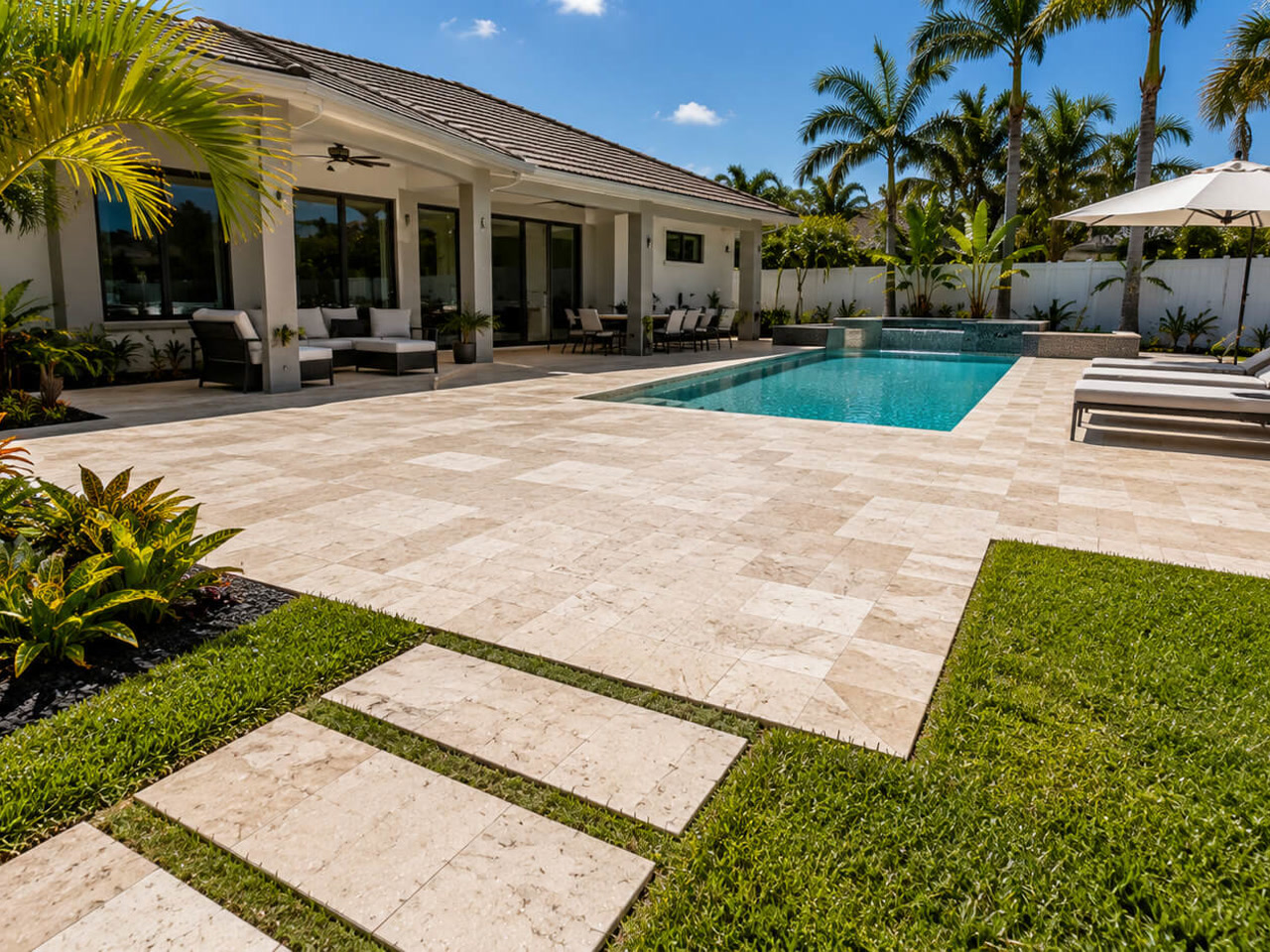 Travertine paver patio beside a pool with a stepping stone walkway leading to the lawn on a Hypoluxo property