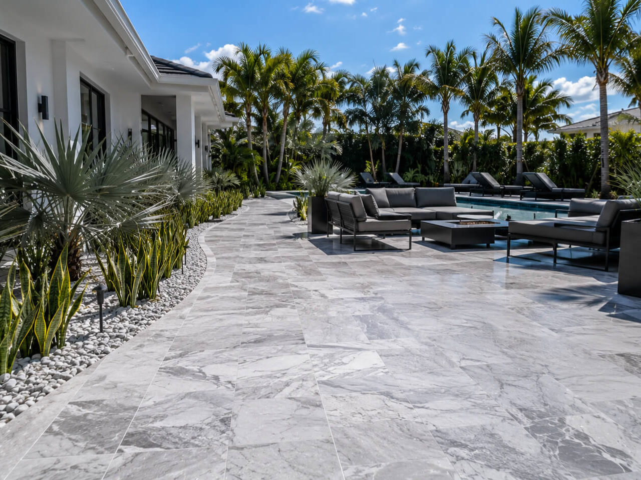 Gray marble paver patio curving along a modern home to a poolside lounge with a fire table at a Jupiter Island estate