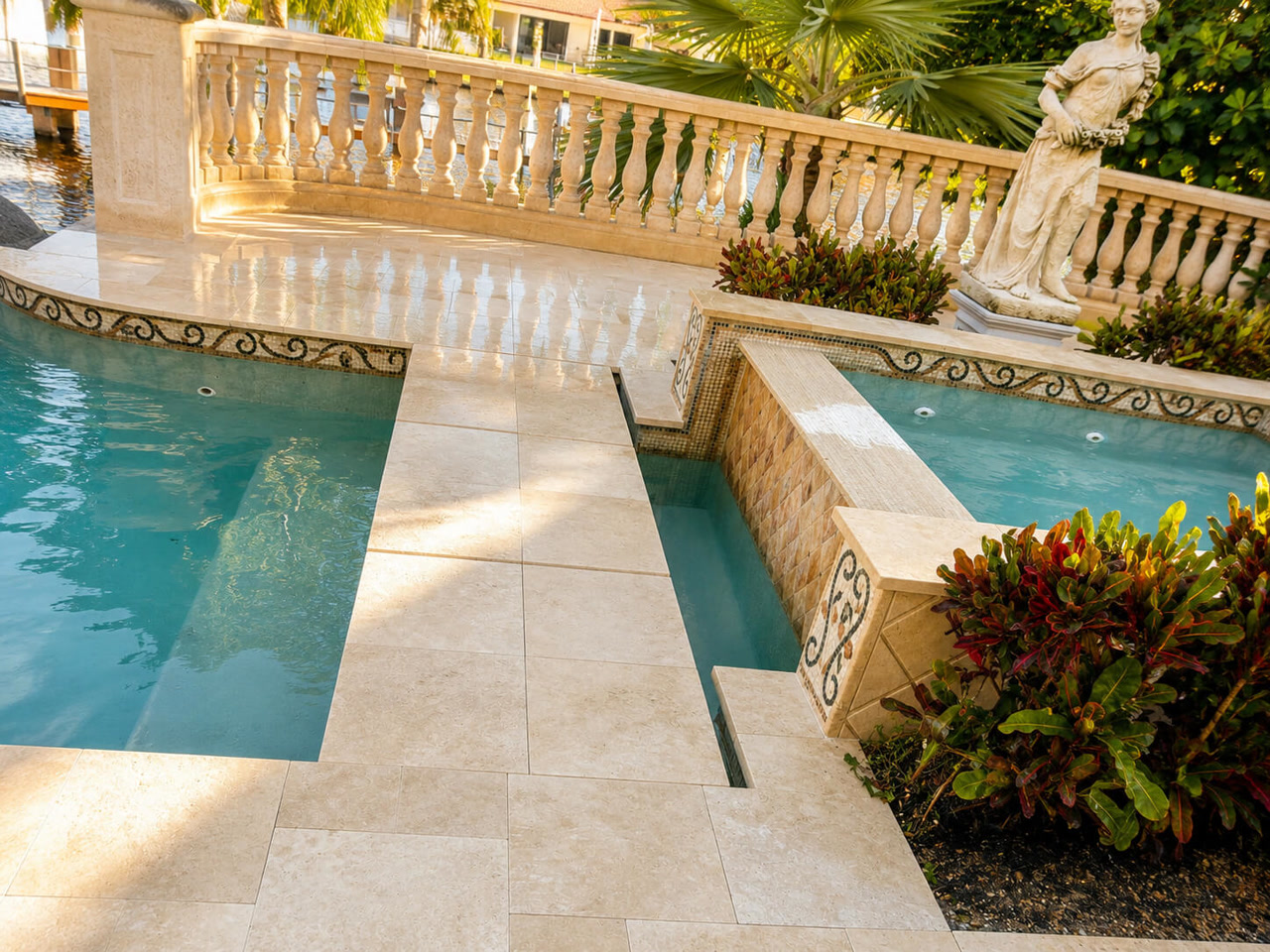 Ivory paver pool deck with a stone balustrade and mosaic tile spillway at a Coconut Creek waterfront estate