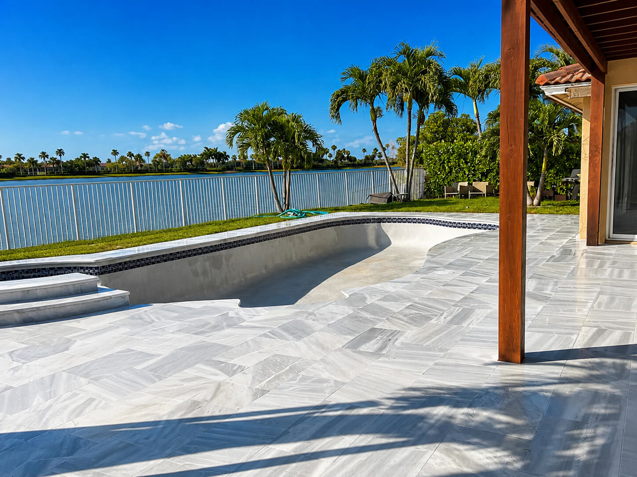 Pool under construction with the new white marble paver deck already installed for a Gulfstream homeowner, overlooking a lake