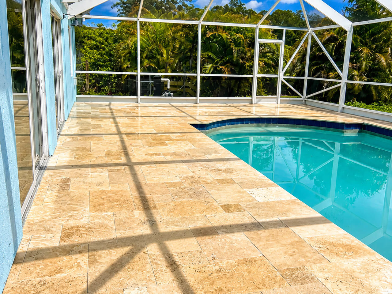 Sand toned travertine paver pool deck under a white screen enclosure at a Jupiter Island estate, with dark blue tile coping along the pool