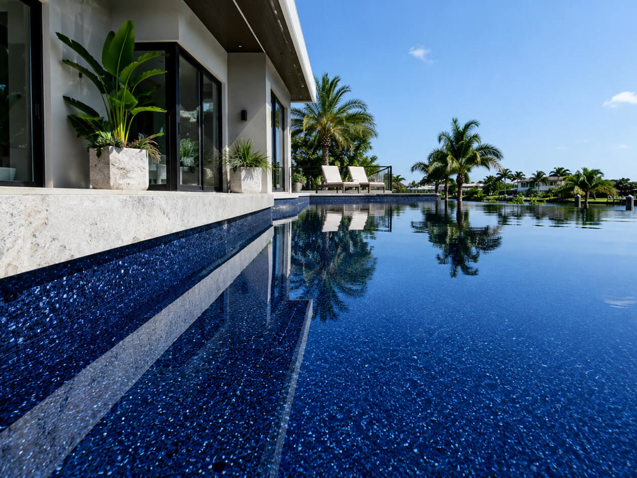 Finished pool resurfacing in a dark pebble finish, with sheer descents spilling in over gray marble coping at a Juno Beach home