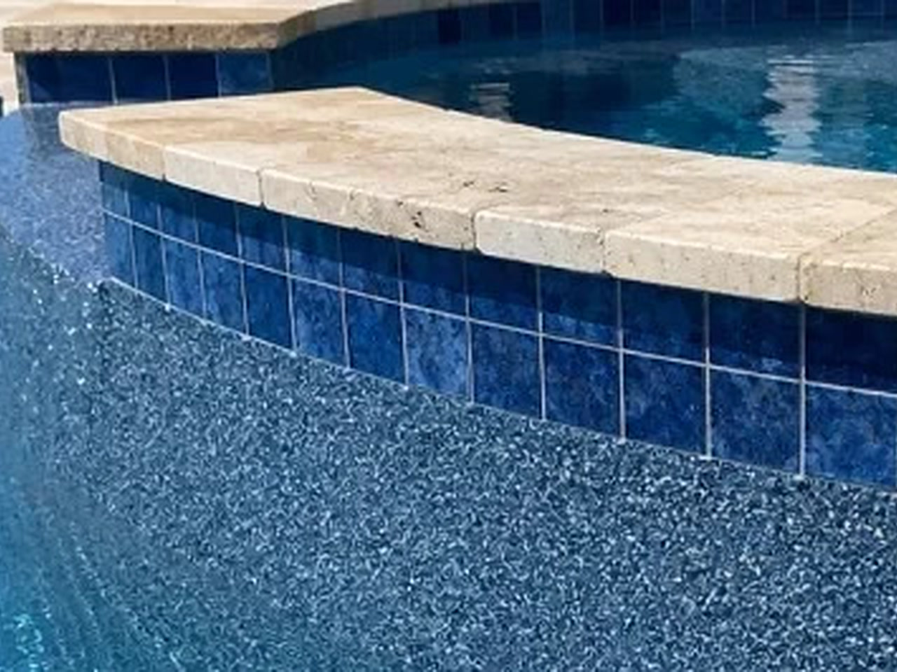 Blue pebble finish meeting a raised spa wall of deep blue tile capped with travertine coping at a Jupiter Island residence