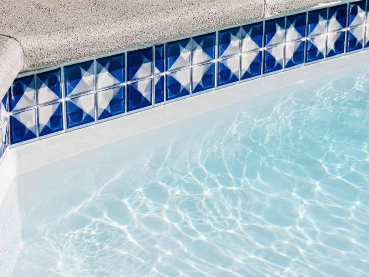 Classic white plaster finish under a blue and white diamond patterned tile border and textured concrete coping for a Lake Worth Beach homeowner