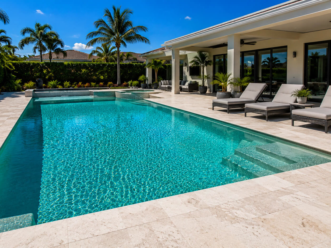 Resurfaced rectangular pool with an integrated spa and travertine deck behind a Pompano Beach home