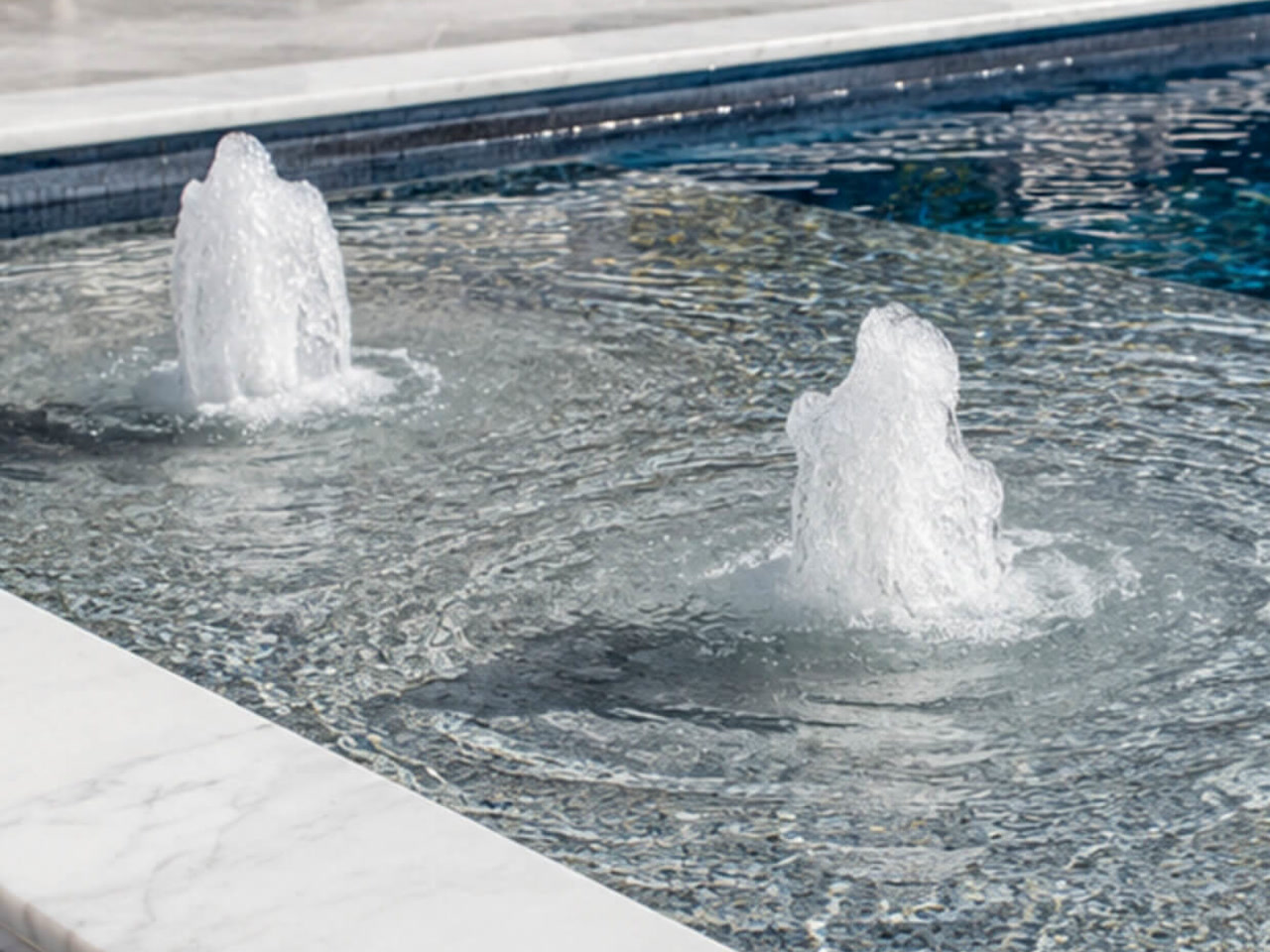 Two bubbler fountains on a mosaic tiled sun shelf edged with white marble coping in a Lake Worth Beach backyard