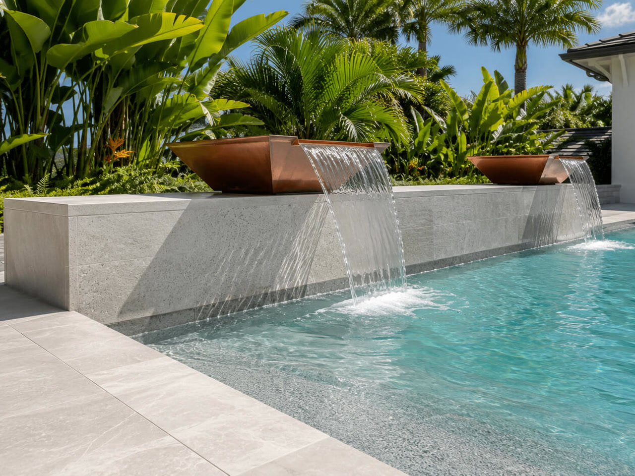 Copper scupper bowls spilling over a light stone wall into a pool framed by tropical planting for a Parkland homeowner