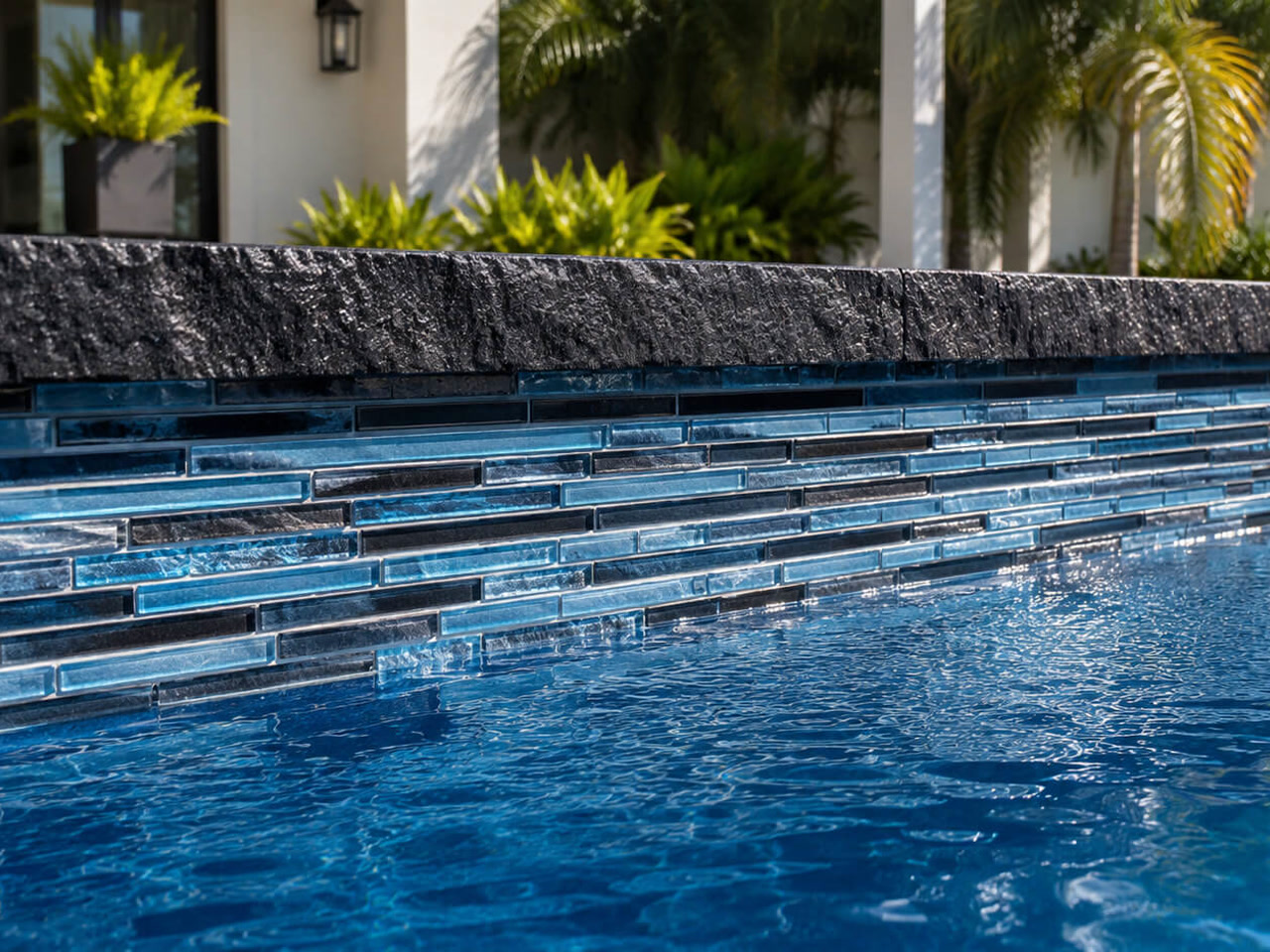 Rough cut black stone coping over linear blue glass waterline tile at a finished Jupiter pool edge