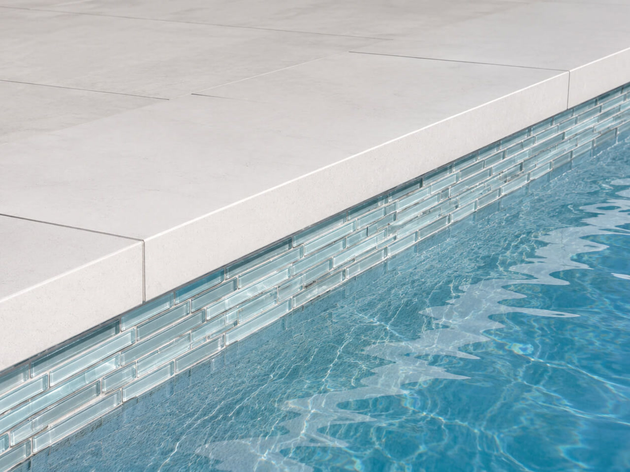 Pool coping in squared off light stone over a linear pale blue glass waterline tile band at a Wellington residence