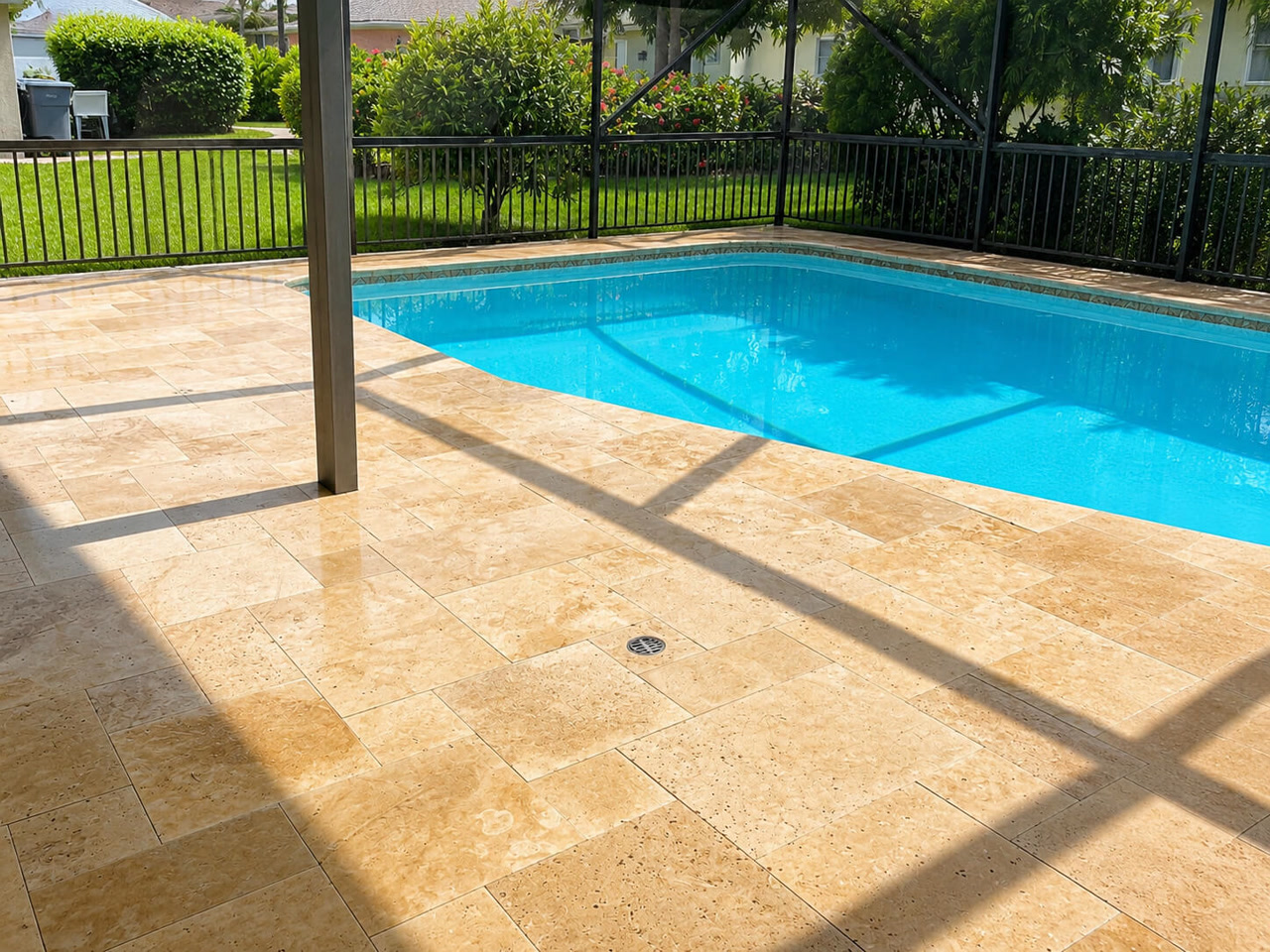 Golden travertine paver pool deck inside a screened lanai, with a fenced backyard beyond the enclosure